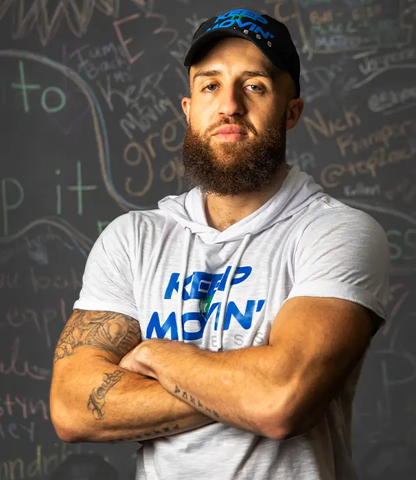 Lead trainer Dante puchala pictured with arms crossed in front of a chalk board wearing a Keep It Movin' Fitness hat and shirt
